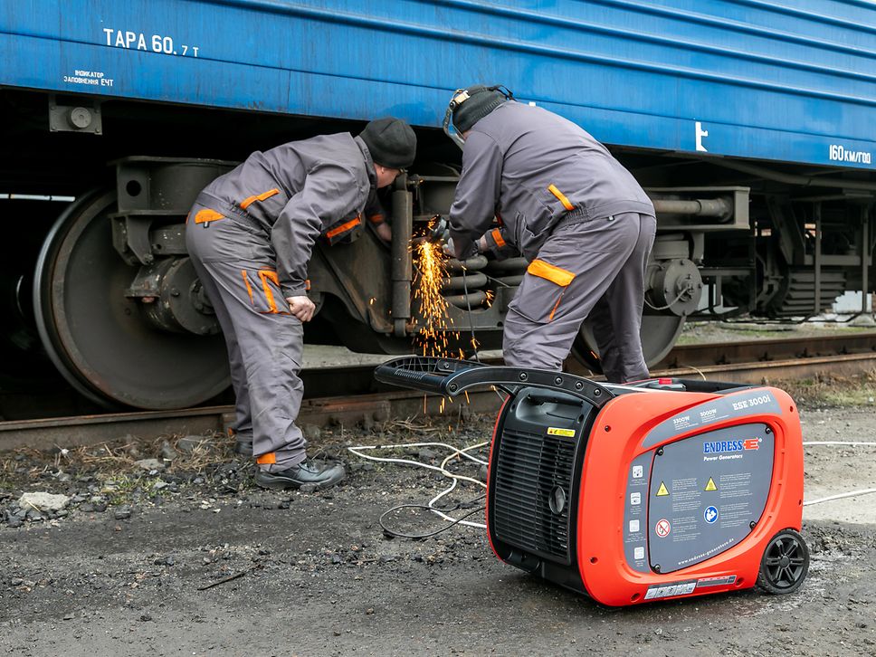 Zwei ukrainische Kollegen führen Schweißarbeiten an einem ukrainischen Zug durch. Im Vordergrund ein Generator.