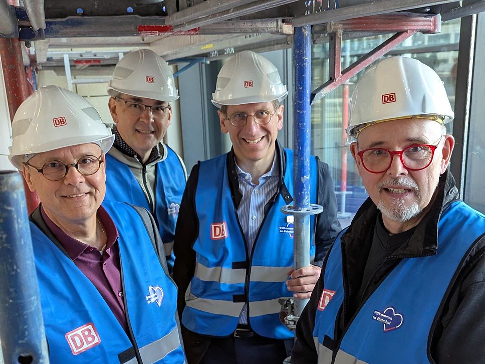 André Seppelt, Stefan Rosemann, Tim Hahlen und Kai Rossmann stehen auf einem Gerüst vor der Anzeigetafel im Bahnhof