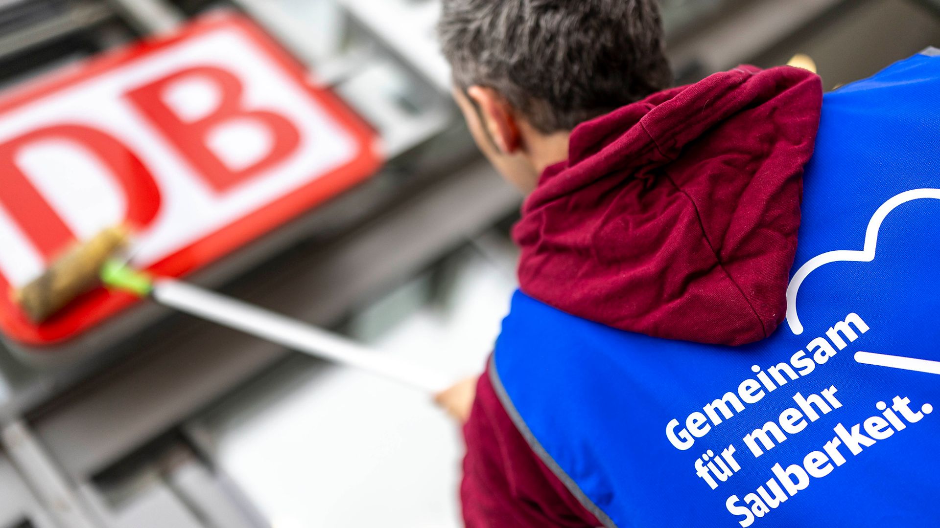 Ein DB-Mitarbeiter putzt das DB-Logo über dem Bahnhofseingang 
