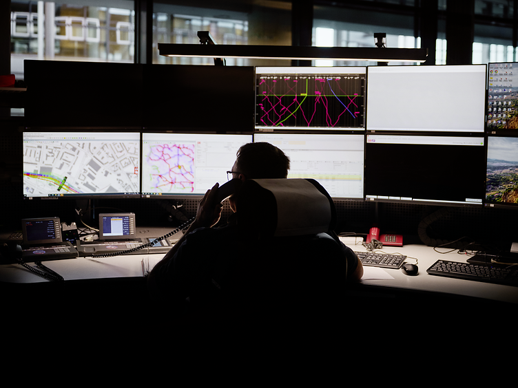 ein Mann schaut im Stellwerk auf Monitore und telefoniert dabei
