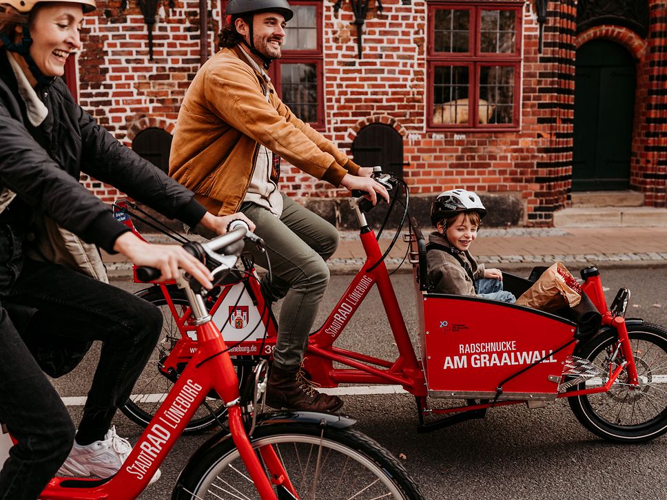 A man rides an electric cargo bike from StadtRad Lüneburg. A child is sitting in the front basket.