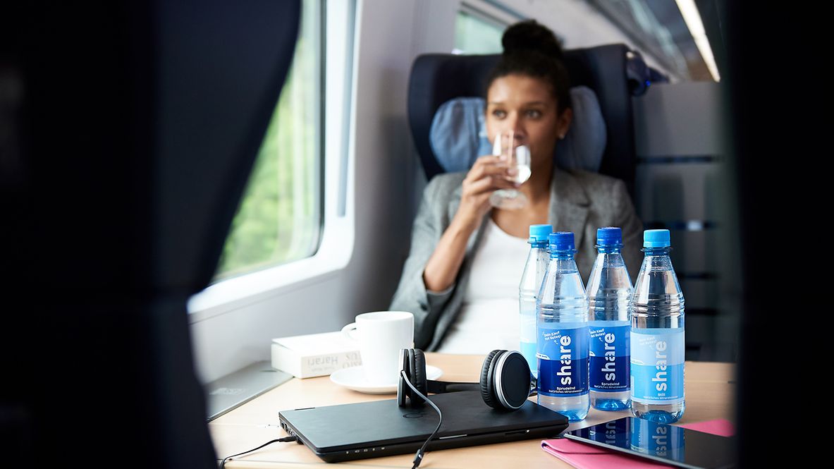 A passenger drinks water from a share bottle on a DB train.