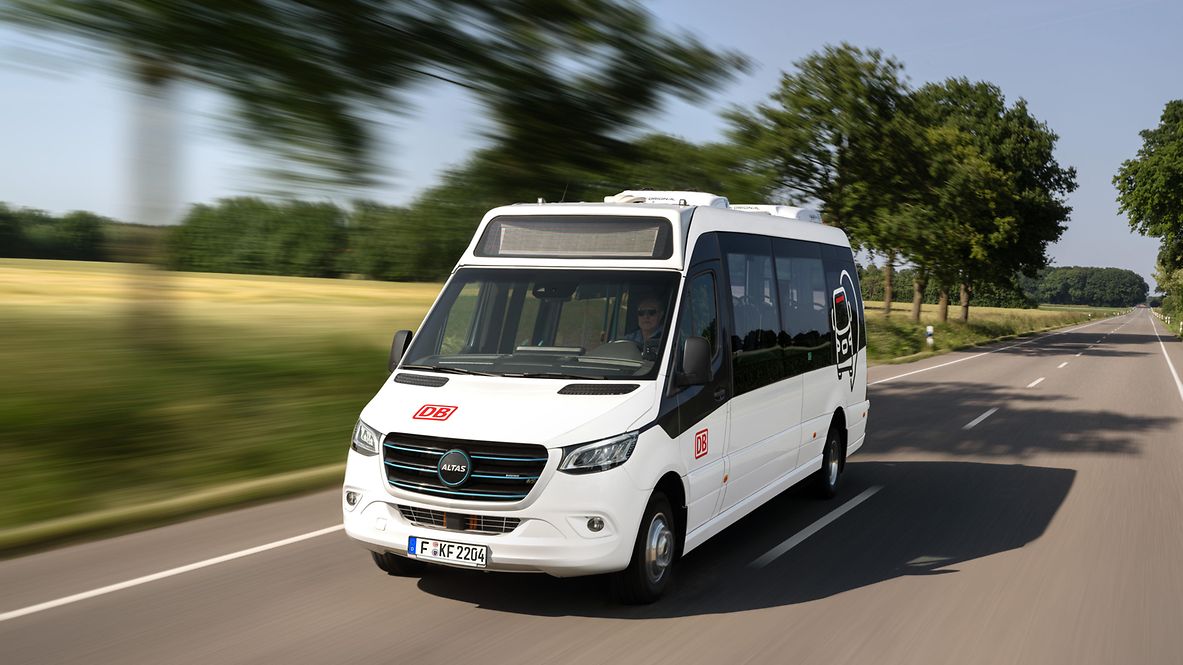A white minibus with DB branding drives along a country road.