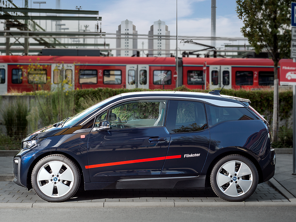 ein Flinkster-Auto, im Hintergrund eine Regionalbahn